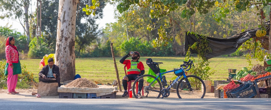 A cyclist stopping beside a roadside vegetable stall during a brevet.